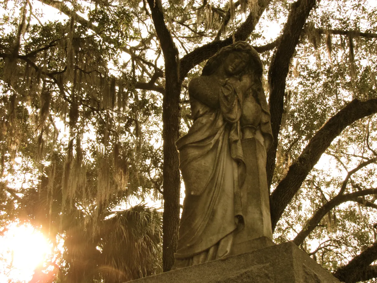 A mourning statue under Spanish moss in Bonaventure Cemetery, a stop beloved by Savannah GA ghost tour fans